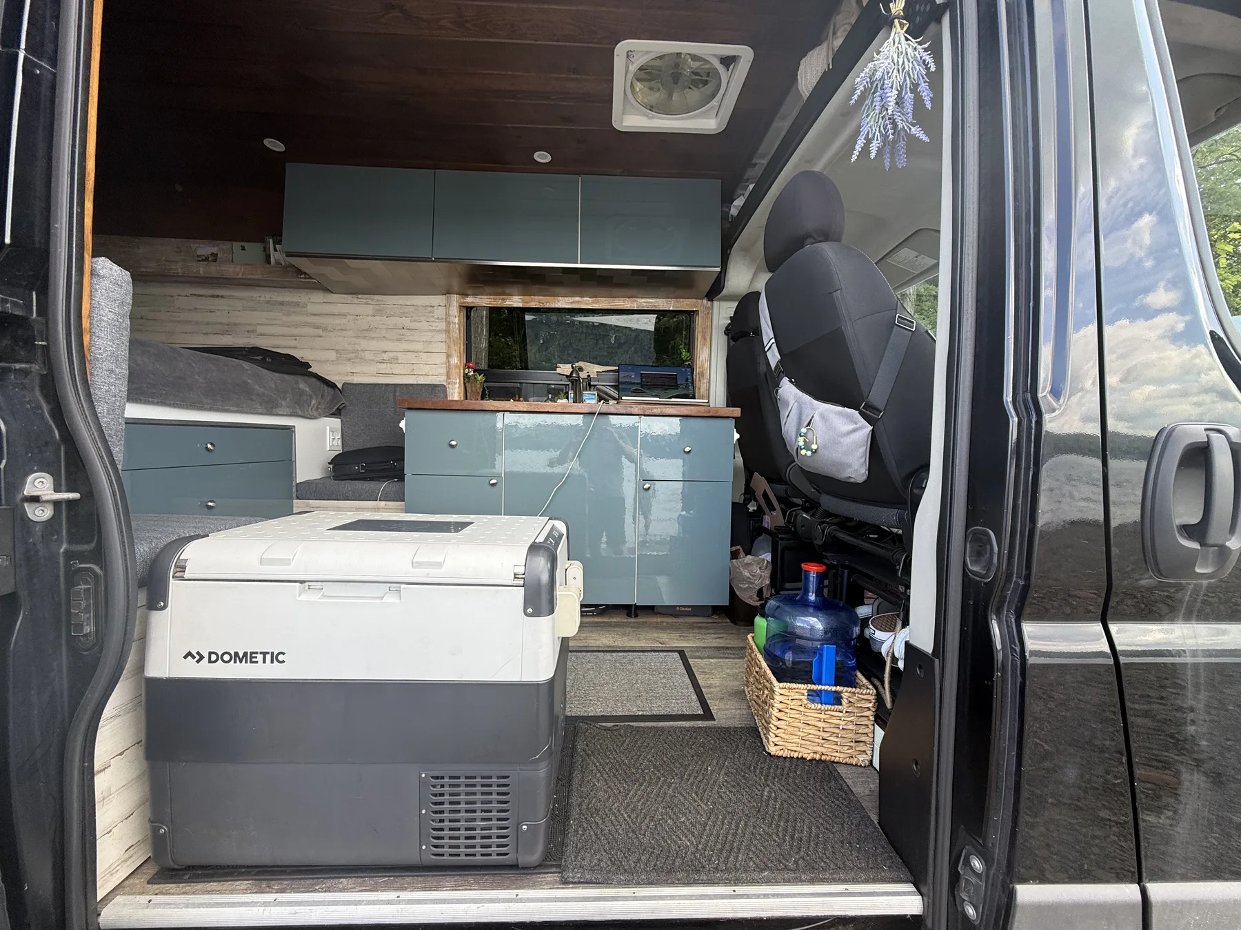 Our Dometic chest fridge sitting on the floor just inside the ProMaster's sliding door, with the galley cabinets, counter and bed behind it