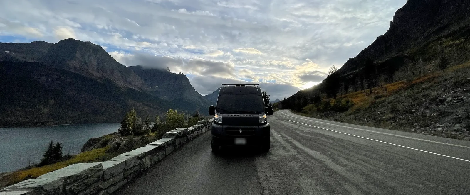 Our ProMaster on a mountain road at dusk, lake on one side and cliffs on the other, one of the views eight years on the road has earned us