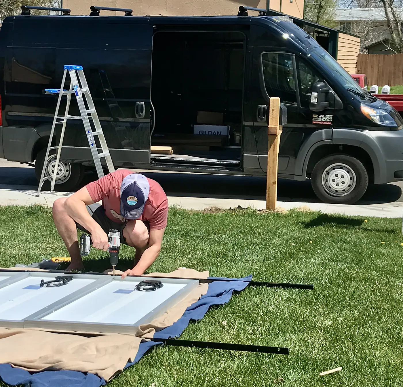 Jesse assembling a solar panel mount on the grass beside the black ProMaster van